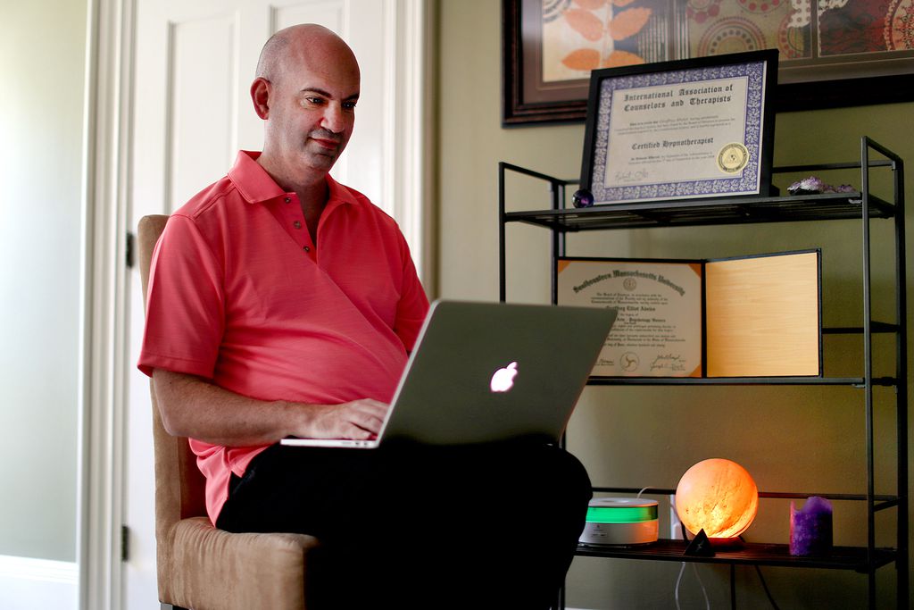 Man seating with laptop on his lap working from home.