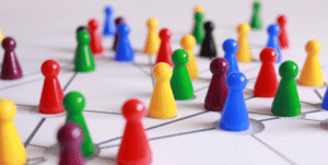 Colourful plastic game pieces representing people are strewn across a white table. Webbed lines connect them in a large network.
