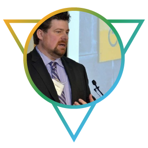 A staff photo of Jeff Wilson. Jeff is a mature Caucasian man with short brown hair and trimmed beard. He appears speaking at an advocacy event, and is wearing a suit and tie.